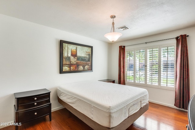 bedroom featuring a textured ceiling, wood finished floors, visible vents, and baseboards