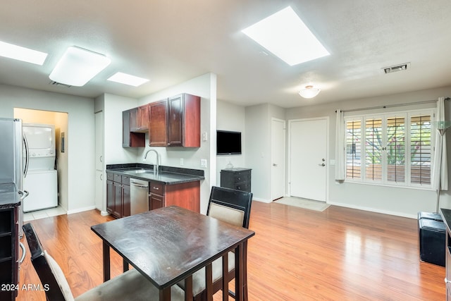 kitchen featuring dark countertops, stacked washer / dryer, visible vents, dishwasher, and a sink