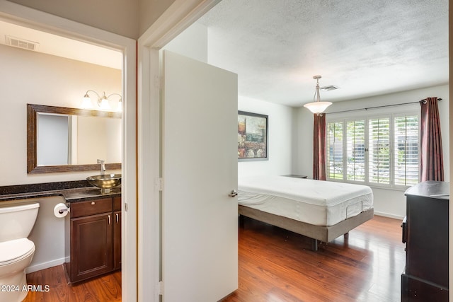 bedroom featuring visible vents, a textured ceiling, baseboards, and wood finished floors