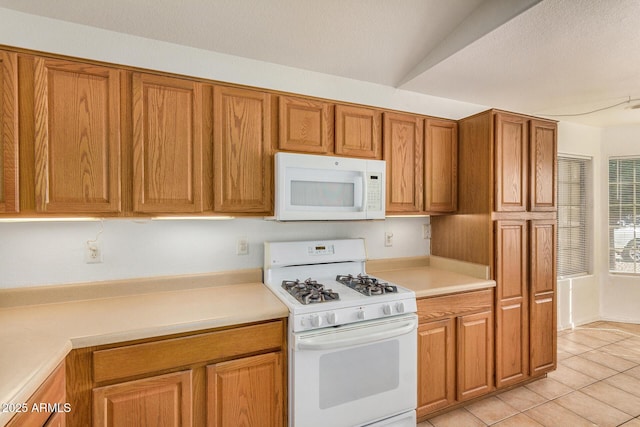 kitchen with white appliances, vaulted ceiling, and light tile patterned flooring