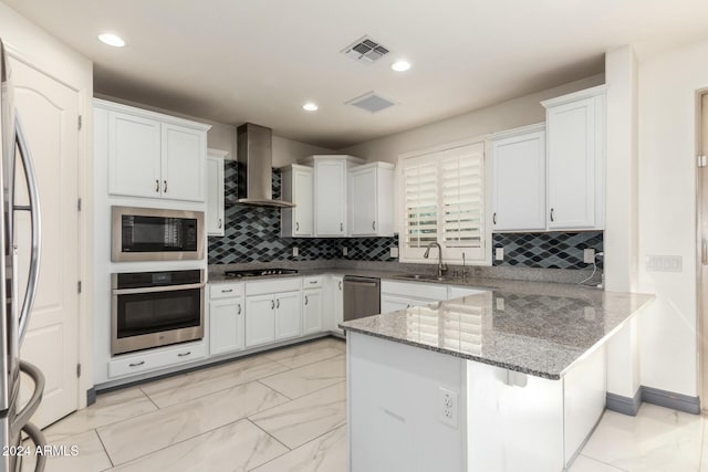 kitchen featuring sink, stainless steel appliances, wall chimney range hood, kitchen peninsula, and white cabinets