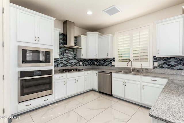 kitchen featuring appliances with stainless steel finishes, white cabinetry, wall chimney exhaust hood, and sink