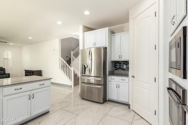 kitchen with white cabinets, light stone counters, appliances with stainless steel finishes, and tasteful backsplash