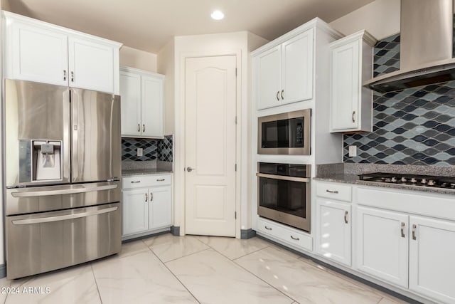 kitchen featuring decorative backsplash, stainless steel appliances, white cabinetry, and wall chimney exhaust hood