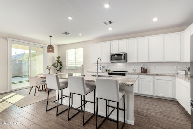 kitchen featuring appliances with stainless steel finishes, decorative light fixtures, sink, white cabinets, and a kitchen island with sink