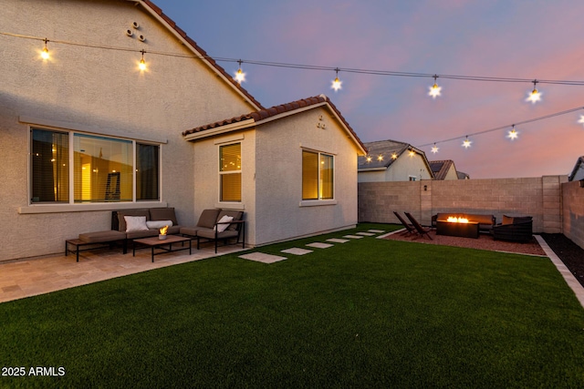 back house at dusk with a patio, a lawn, and an outdoor living space with a fire pit