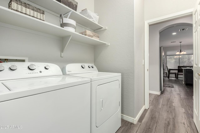 laundry area with washing machine and clothes dryer, a chandelier, and light hardwood / wood-style floors