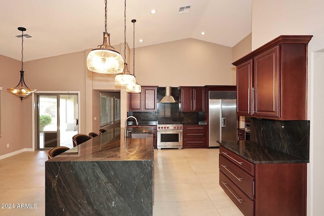 kitchen with wall chimney range hood, tasteful backsplash, an island with sink, pendant lighting, and high end appliances