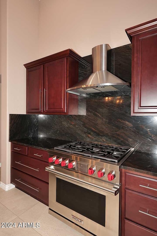 kitchen with tasteful backsplash, luxury range, wall chimney range hood, light tile patterned floors, and dark stone countertops