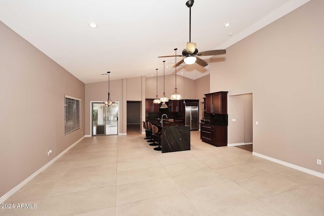 kitchen featuring a kitchen breakfast bar, dark brown cabinets, ceiling fan with notable chandelier, a kitchen island with sink, and stainless steel fridge with ice dispenser