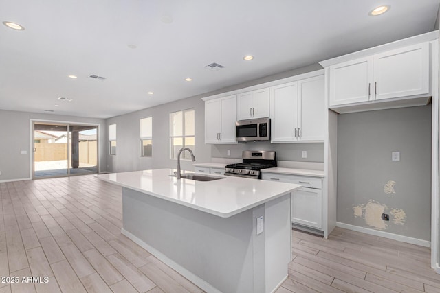 kitchen with a wealth of natural light, visible vents, an island with sink, a sink, and appliances with stainless steel finishes