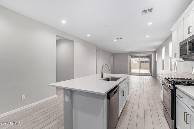 kitchen with visible vents, a center island with sink, a sink, stainless steel appliances, and wood tiled floor