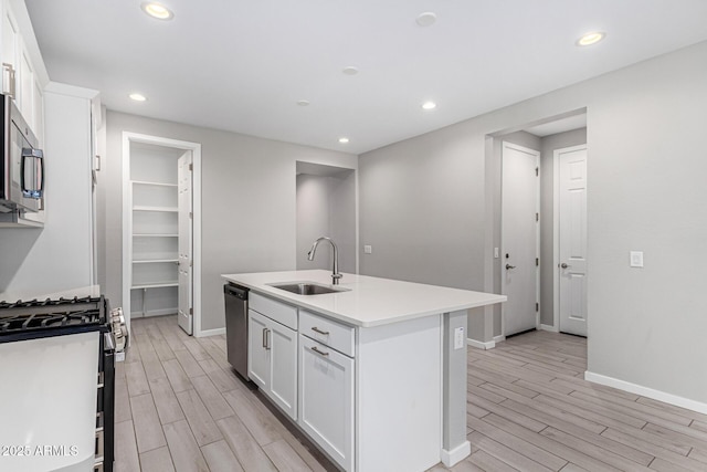 kitchen with a center island with sink, stainless steel appliances, wood finish floors, and a sink