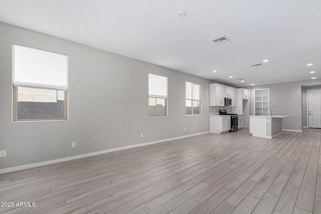 unfurnished living room featuring baseboards, light wood-style floors, and a sink