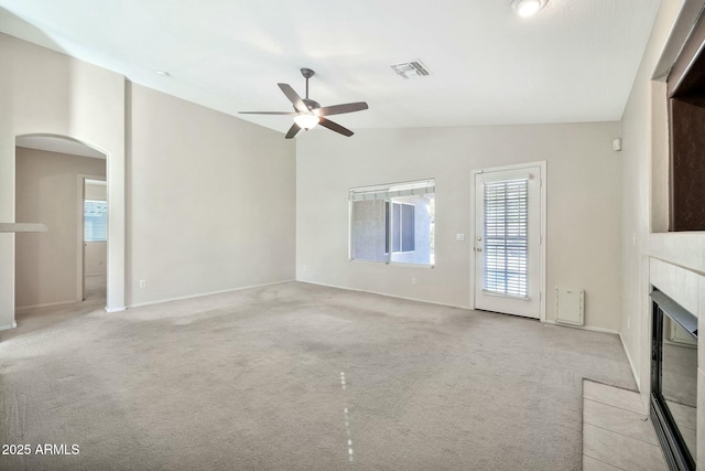 unfurnished living room with ceiling fan, light colored carpet, lofted ceiling, and a tiled fireplace