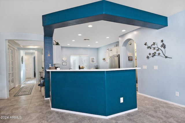 kitchen featuring stainless steel fridge, kitchen peninsula, light tile patterned flooring, and white cabinets