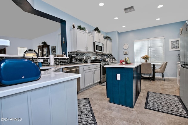 kitchen featuring a center island, white cabinets, kitchen peninsula, appliances with stainless steel finishes, and backsplash