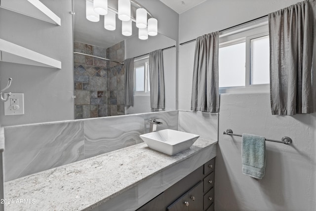 bathroom with a healthy amount of sunlight, a tile shower, and vanity