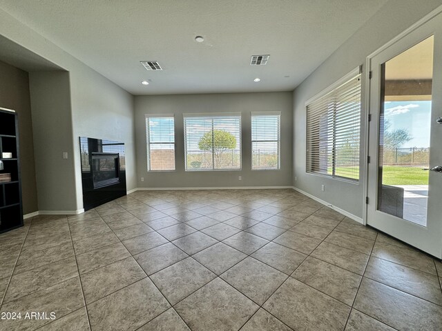 unfurnished living room featuring light tile patterned floors, a textured ceiling, a wood stove, and a wealth of natural light