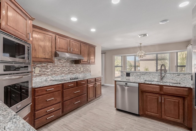 kitchen featuring appliances with stainless steel finishes, decorative light fixtures, light stone counters, and sink