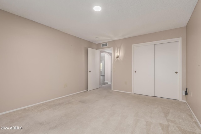 unfurnished bedroom featuring light carpet, a closet, and a textured ceiling