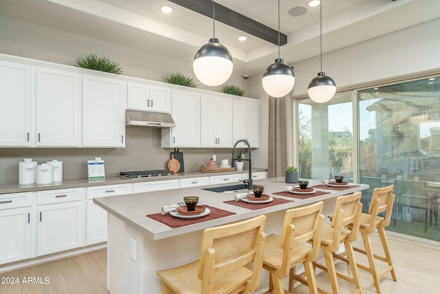 kitchen featuring a center island with sink, pendant lighting, white cabinetry, and a breakfast bar area