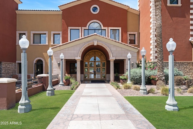view of exterior entry with a lawn, french doors, and stucco siding