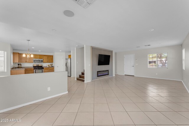 unfurnished living room featuring visible vents, a glass covered fireplace, light tile patterned flooring, baseboards, and a sink