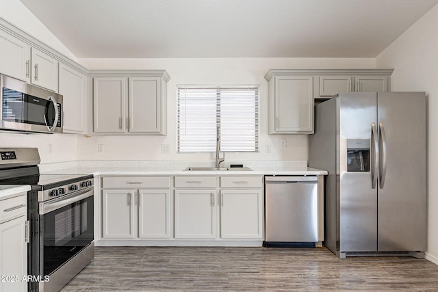 kitchen featuring appliances with stainless steel finishes, light countertops, a sink, and wood finished floors