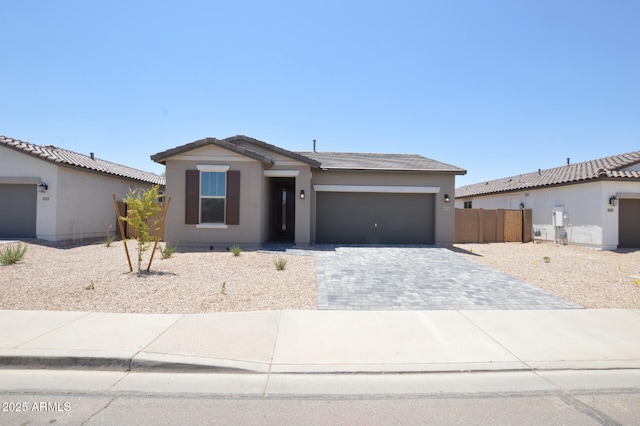 ranch-style home featuring an attached garage, fence, decorative driveway, and stucco siding