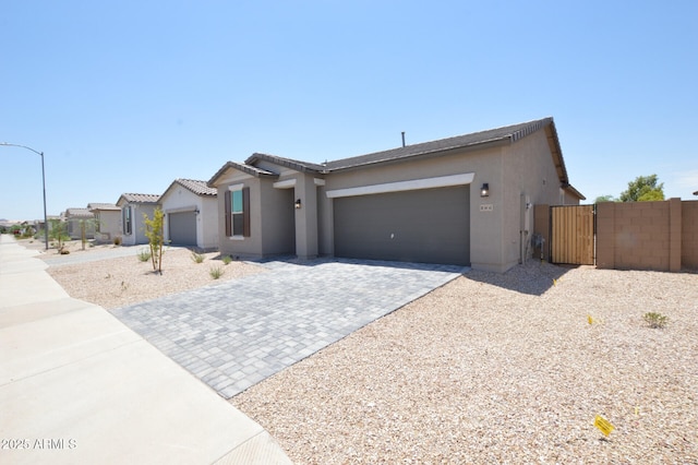 view of front facade with a garage, fence, decorative driveway, a gate, and stucco siding