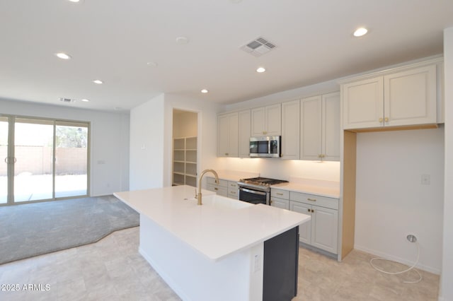 kitchen with light colored carpet, stainless steel appliances, a sink, visible vents, and an island with sink