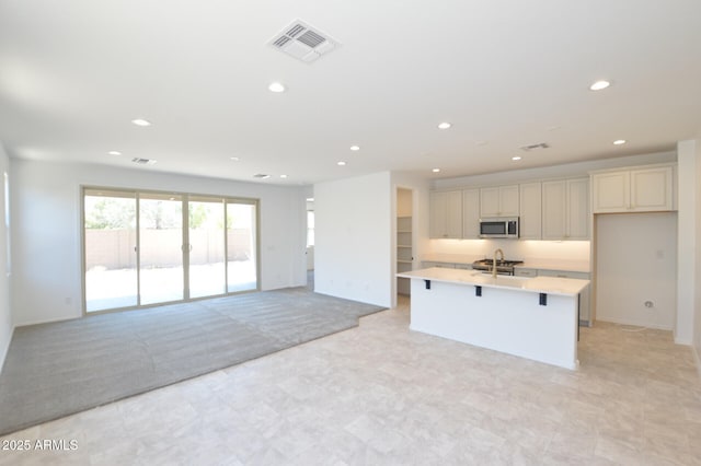 kitchen with a center island with sink, recessed lighting, light countertops, visible vents, and stainless steel microwave