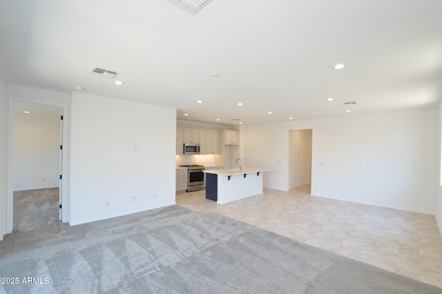 unfurnished living room with visible vents, light colored carpet, a sink, and recessed lighting