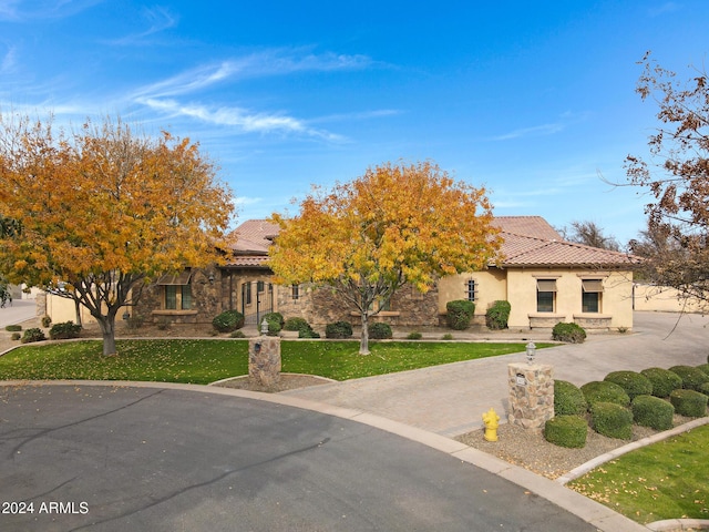 view of front of home featuring a tile roof, driveway, stone siding, stucco siding, and a front lawn