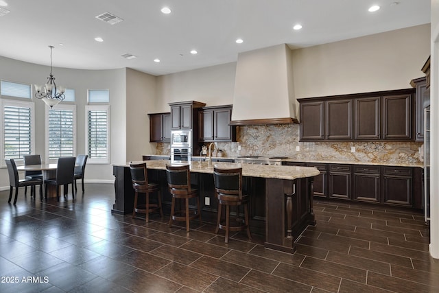 kitchen with a kitchen island with sink, visible vents, dark brown cabinets, appliances with stainless steel finishes, and custom exhaust hood