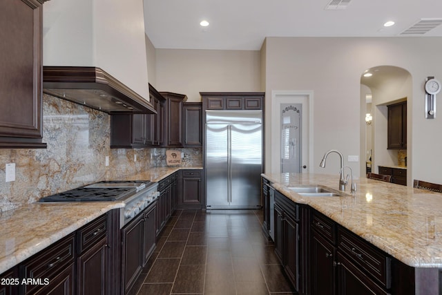 kitchen with custom exhaust hood, tasteful backsplash, appliances with stainless steel finishes, a sink, and dark brown cabinets