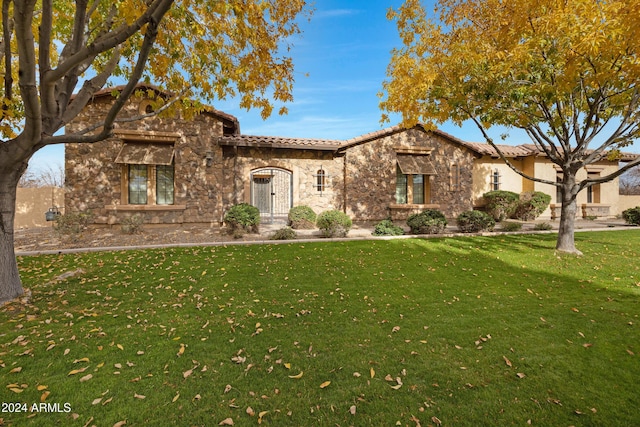 mediterranean / spanish home with stone siding, a tiled roof, and a front yard