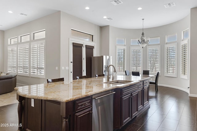 kitchen with stainless steel appliances, visible vents, hanging light fixtures, a sink, and an island with sink