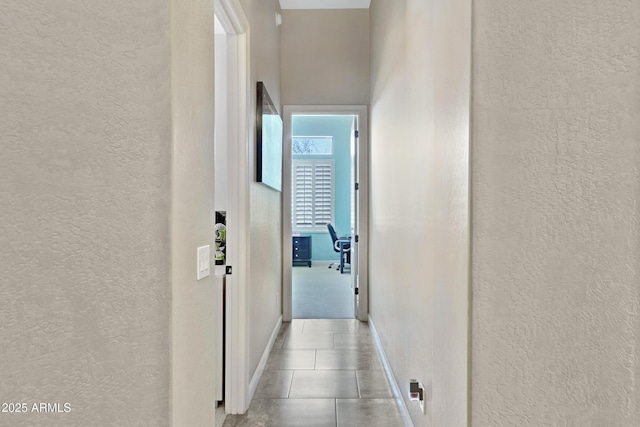 hall with a textured wall, baseboards, and light tile patterned floors