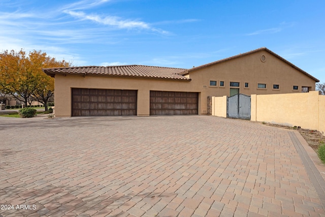 view of front facade featuring decorative driveway, a tile roof, stucco siding, an attached garage, and fence