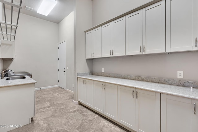 kitchen with baseboards, visible vents, white cabinets, light stone counters, and a sink