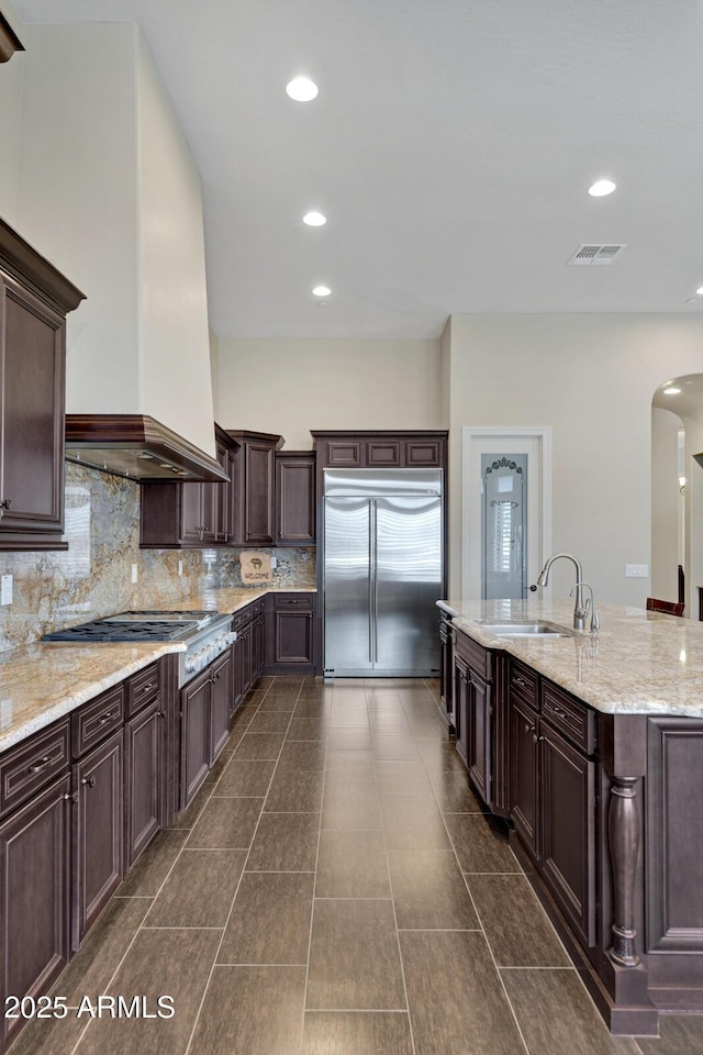 kitchen with custom exhaust hood, stainless steel appliances, visible vents, a sink, and dark brown cabinets