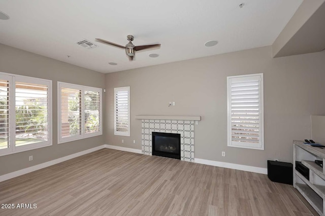 unfurnished living room with a tiled fireplace, visible vents, baseboards, and a ceiling fan