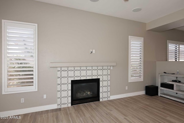 unfurnished living room featuring wood finish floors, baseboards, plenty of natural light, and a tile fireplace
