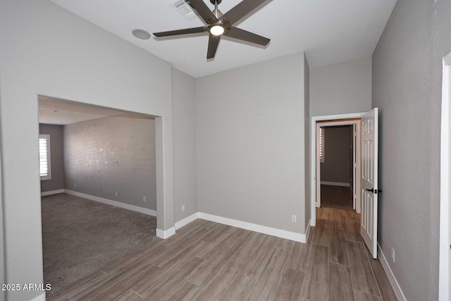 empty room with ceiling fan, visible vents, baseboards, and wood finished floors