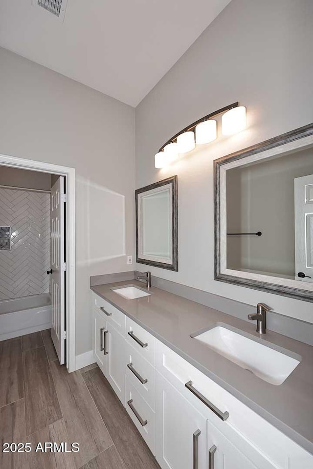 full bathroom featuring double vanity, wood finished floors,  shower combination, and a sink