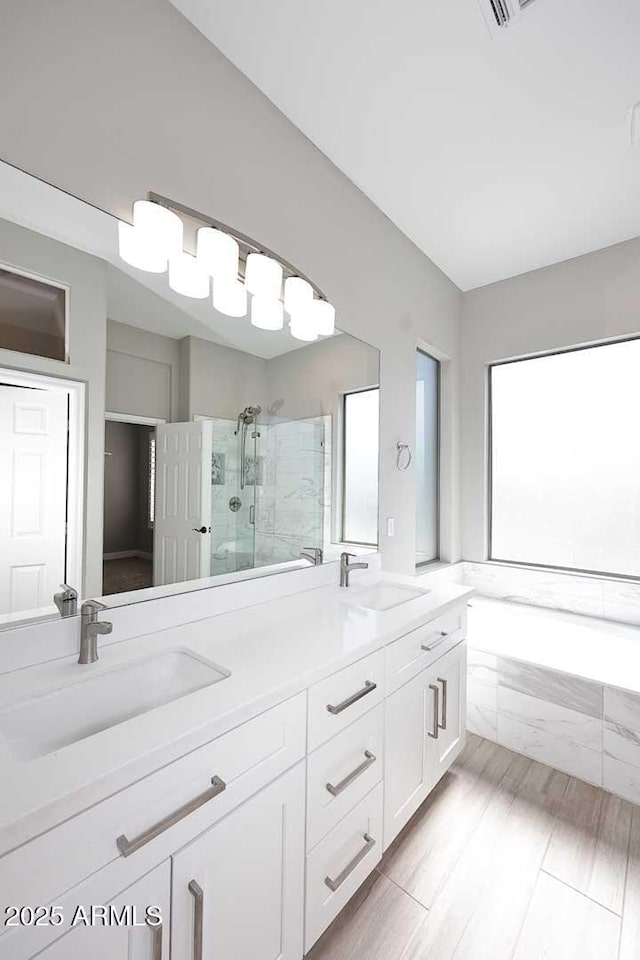 full bathroom featuring double vanity, a stall shower, a bath, and a sink