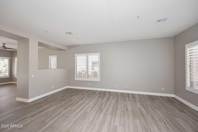 unfurnished room featuring a wealth of natural light, visible vents, baseboards, and wood finished floors