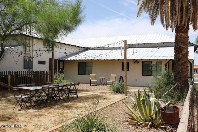 rear view of property featuring a patio, stucco siding, metal roof, fence, and outdoor dining space